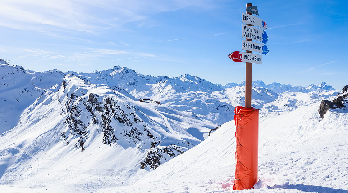 signpost for various mountains and slopes standing in the snow on an epic mountainside with bright blue skies